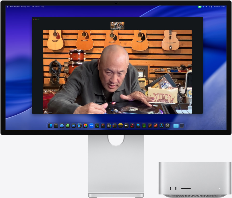 Na Studio Displayi XDR, pod kterým je zasunutý Mac Studio, probíhá videohovor, jehož účastník si v obchodě s hudebními nástroji prohlíží vystavený gramofon