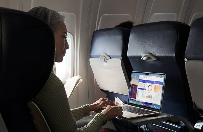 Seseorang bekerja menggunakan MacBook Air saat berada di kursi pesawat